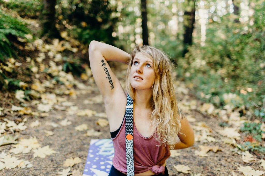 Woman using a yoga stretching strap with metal buckles outdoors in a forest setting.