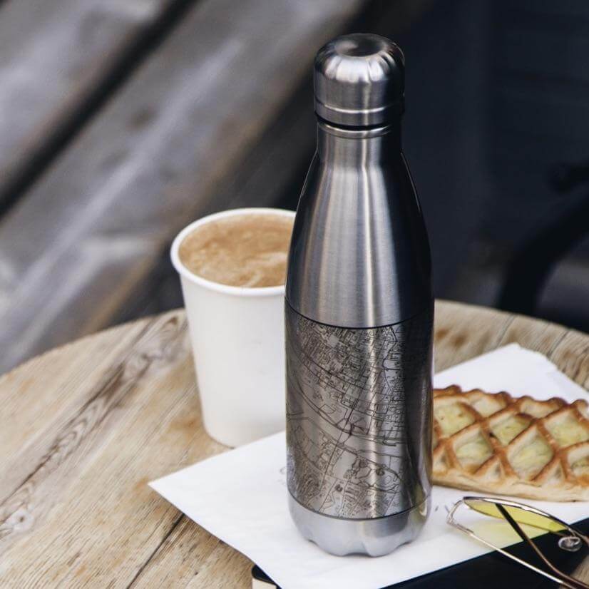Custom engraved Colorado Springs map insulated bottle in matte black, placed on a wooden table next to coffee.