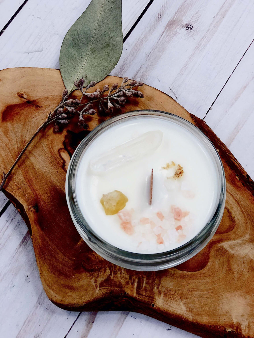 Hand-poured soy wax intention candle on a wooden surface, featuring crystals and natural elements for space cleansing.