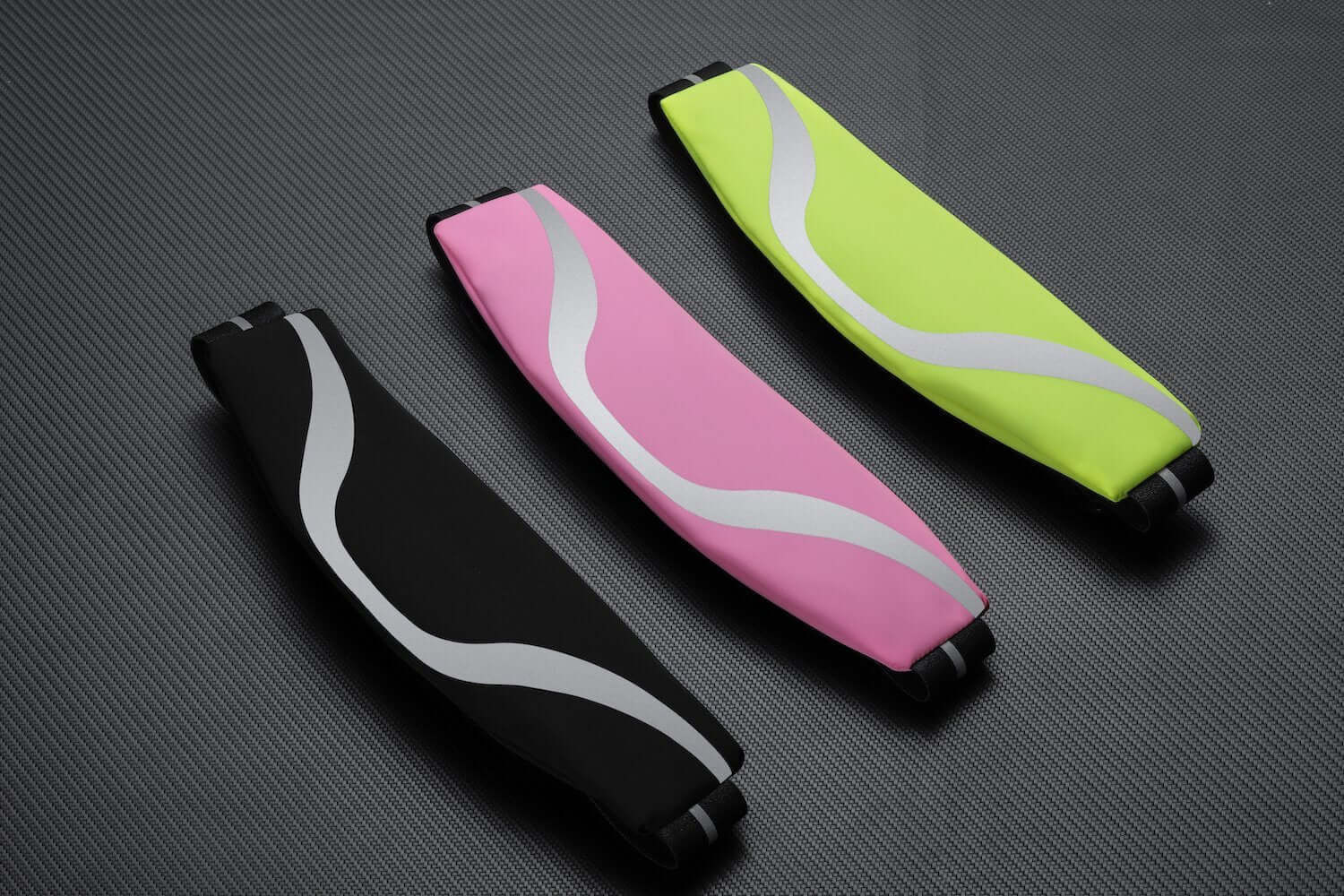 Three water-resistant sport waist packs in black, pink, and yellow with reflective strips on a textured background.