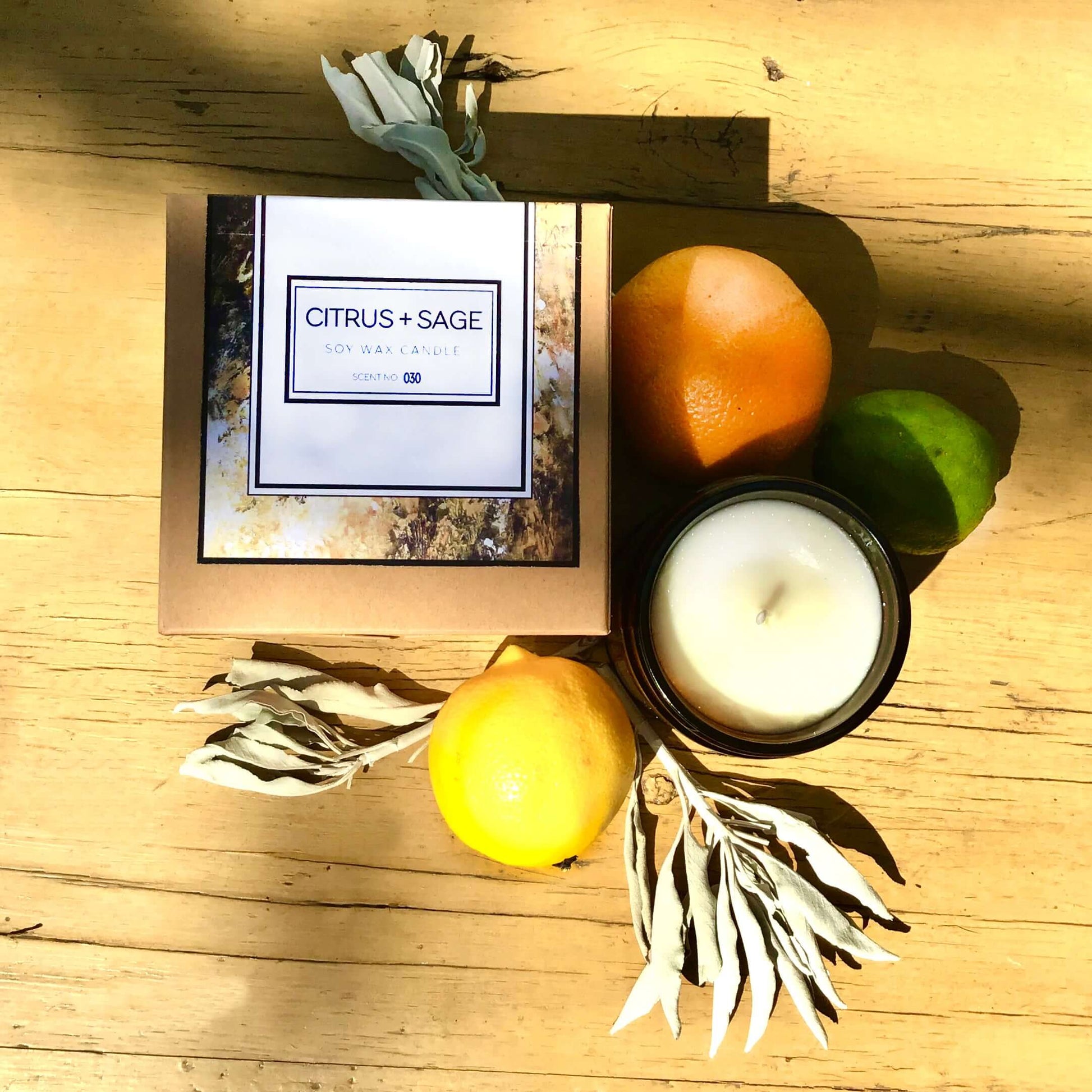 Citrus + Sage Soy Wax Candle with citrus fruits and sage leaves on a wooden table, showcasing its bright aroma and natural ingredients.