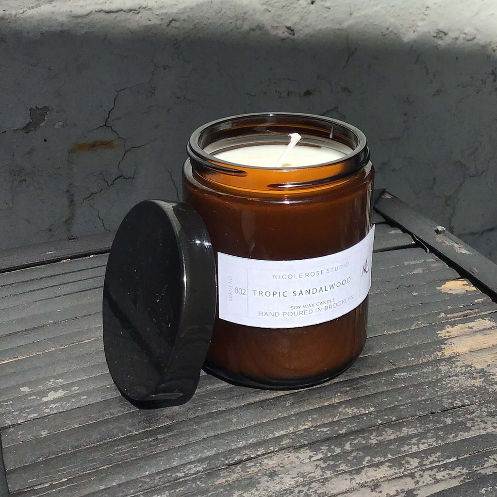 Hand-poured Tropic Sandalwood soy wax candle in an amber glass jar with black lid, showcasing a cozy ambiance.
