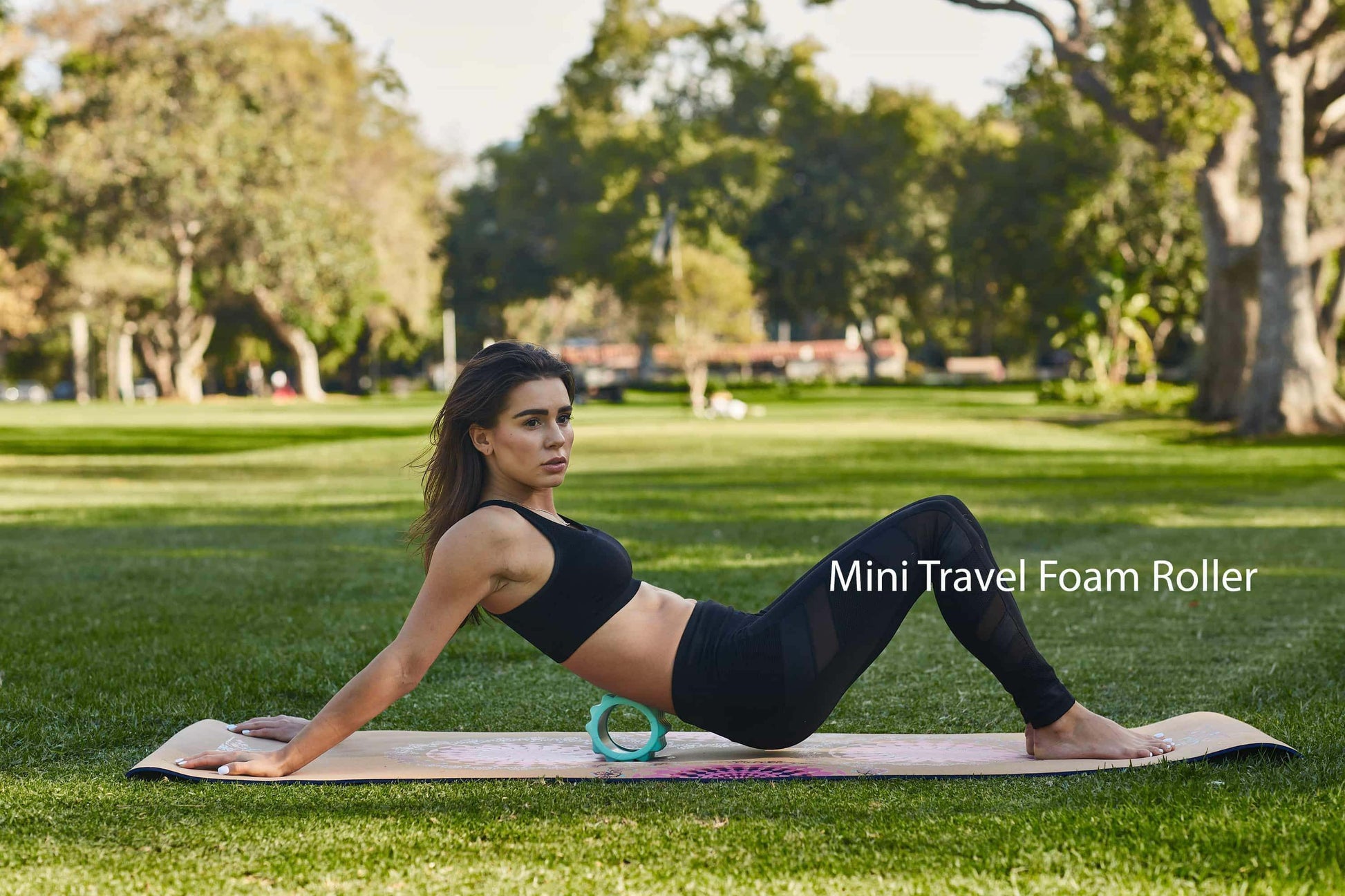 Woman using Mini Travel Foam Roller on yoga mat in park for muscle recovery and flexibility.